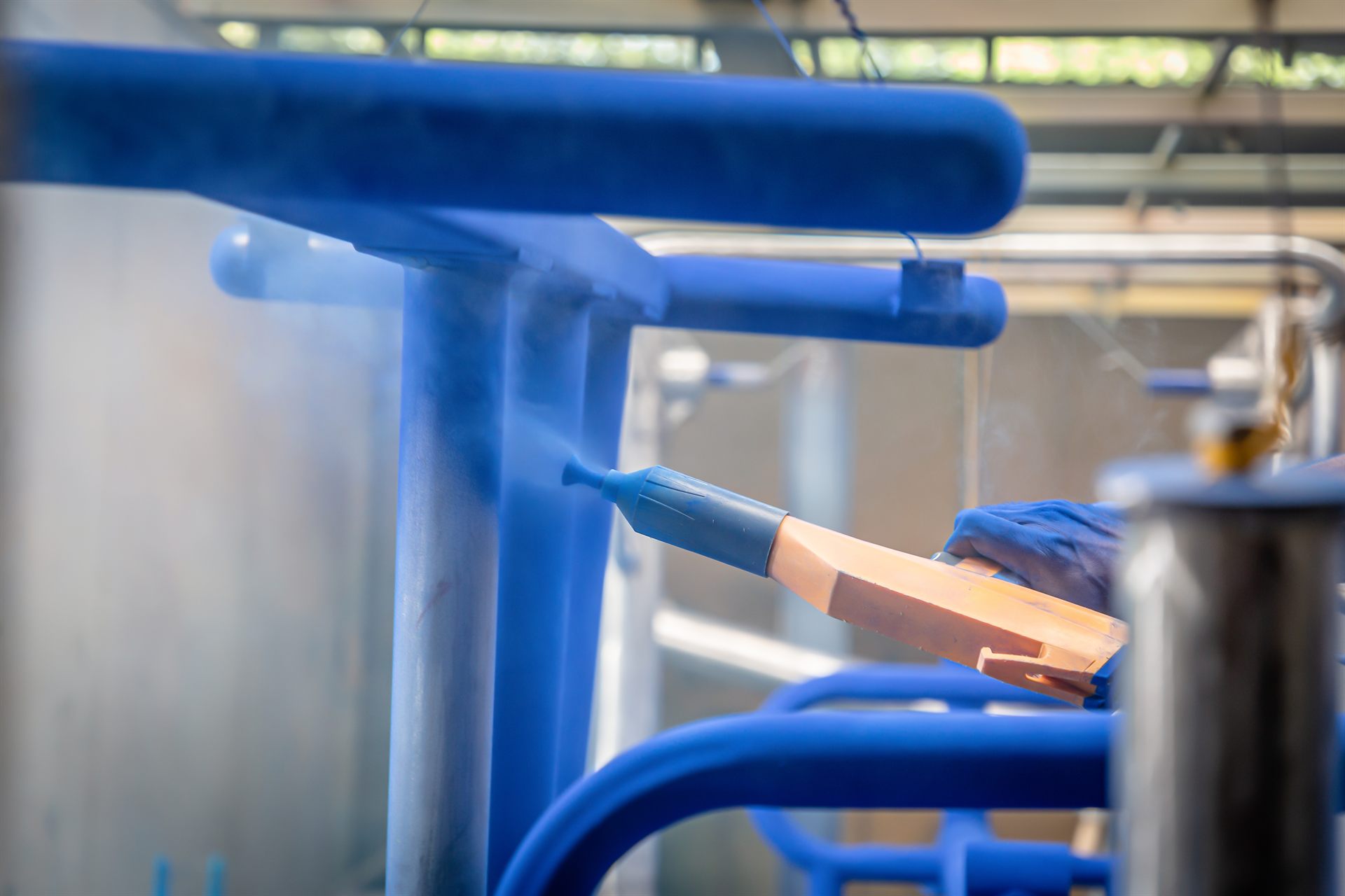 Pulverpistole trägt elektrostatisch aufgeladenes blaues Pulver auf ein hängendes Rohrgestell auf